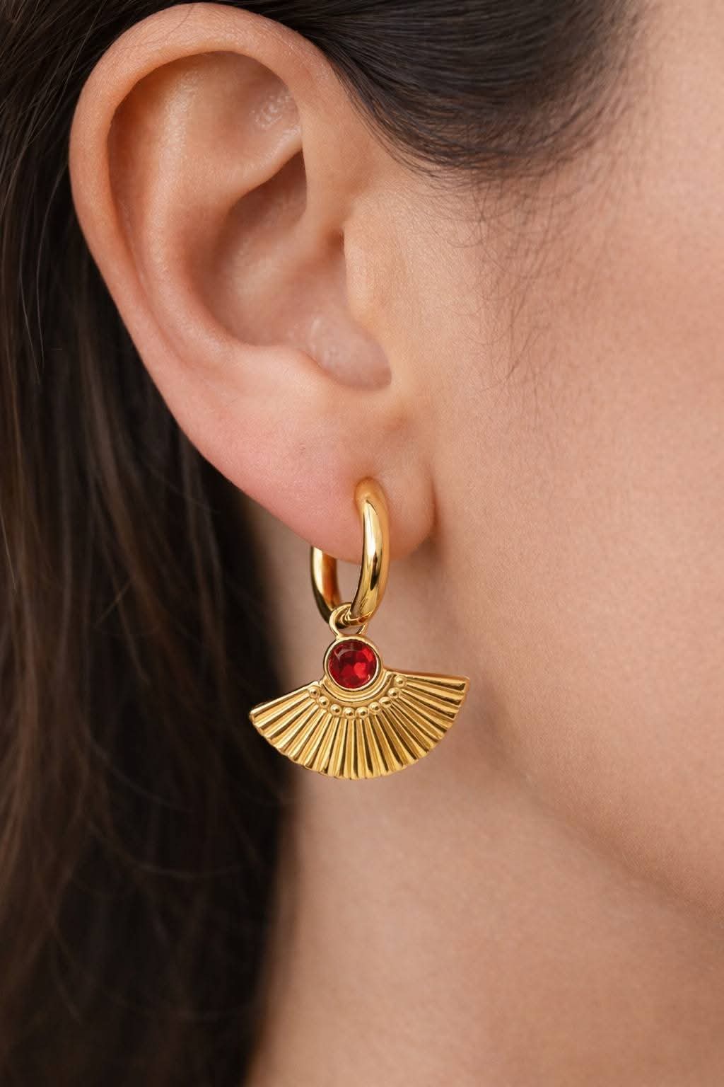 Gold fan earrings with red gemstones worn on an ear