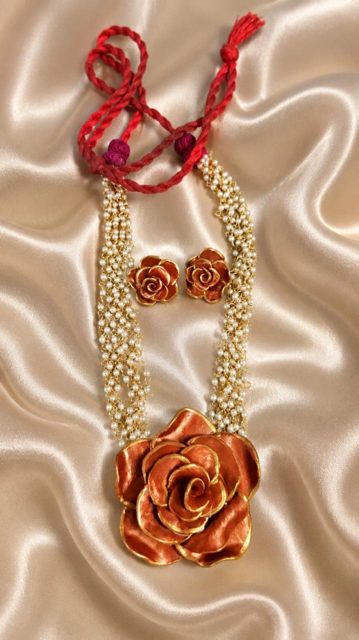 A handmade floral necklace and matching earrings styled on champagne satin